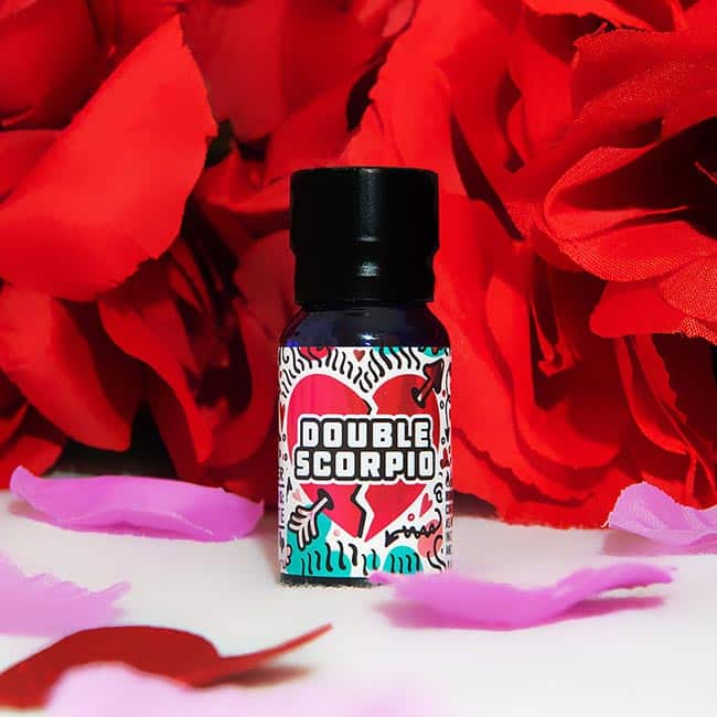 A bottle of Double Scorpio Love Potion - 10ml is set against a vivid backdrop of red faux flowers with scattered pink petals.